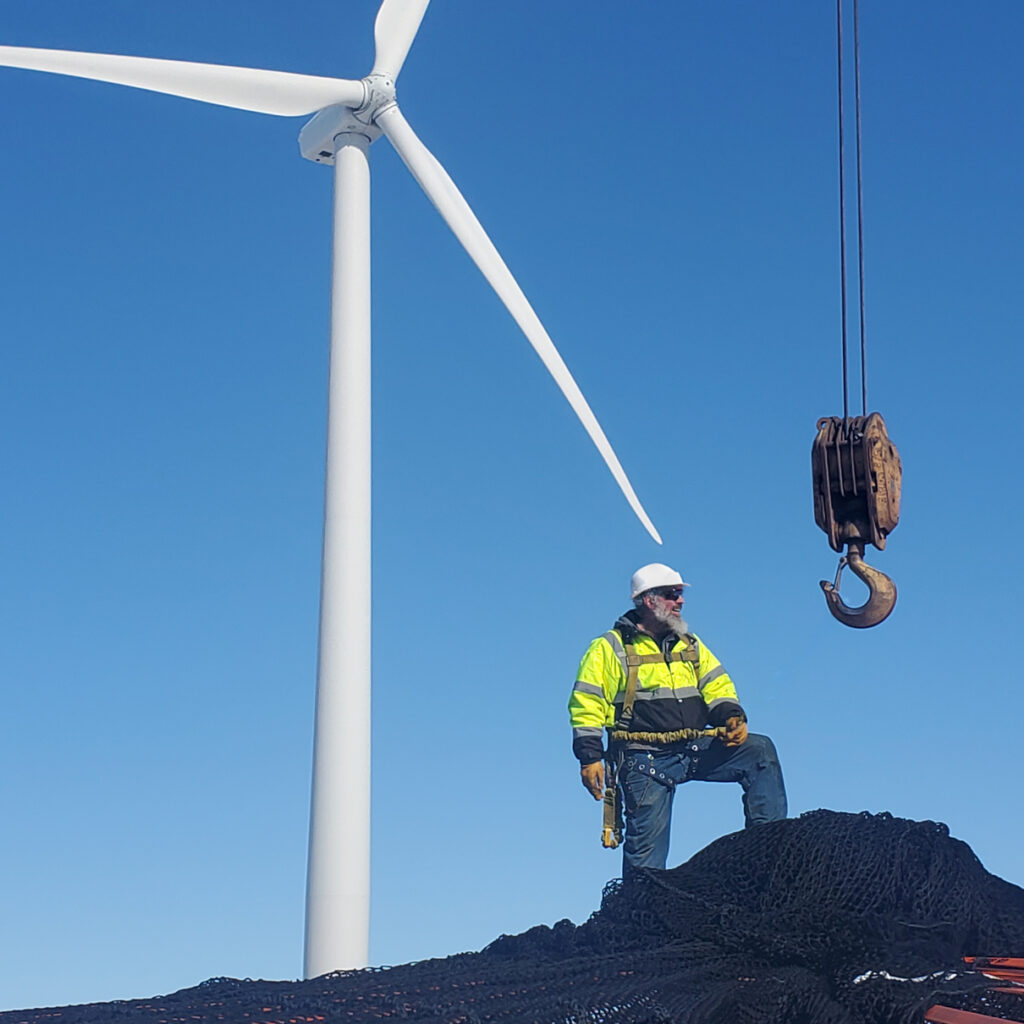 worker with hardhat standing on oile of netting in front of wind turbine